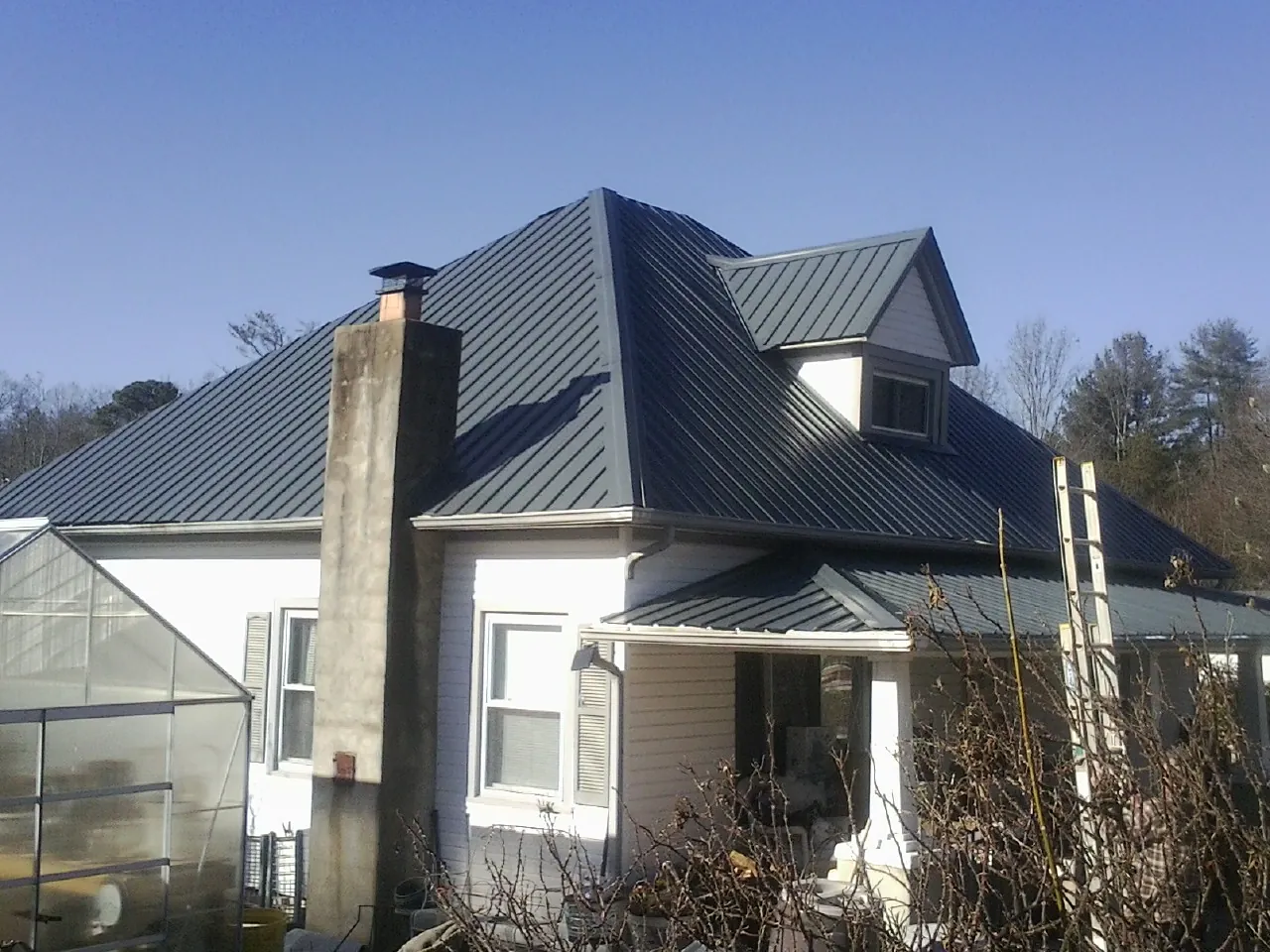 Dark blue standing seam metal roof on a white farmhouse with dormer — Slate & Tile Roof Repair by Roofing Brothers in Purdys