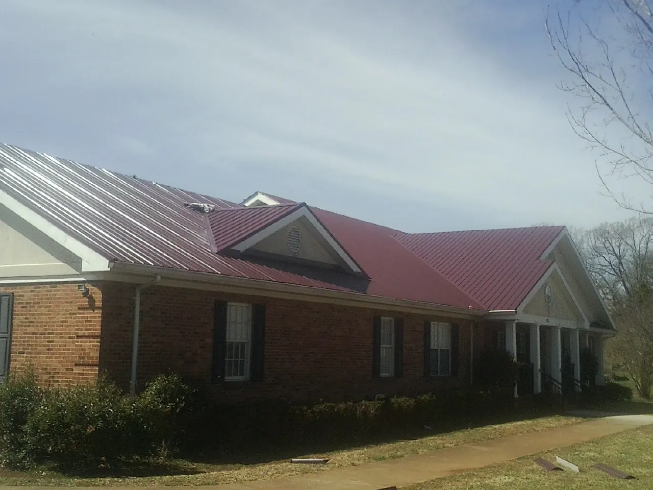 Red metal roof with gabled entries on a long brick building, from a Hail Damage Roof Repair job in Purdys