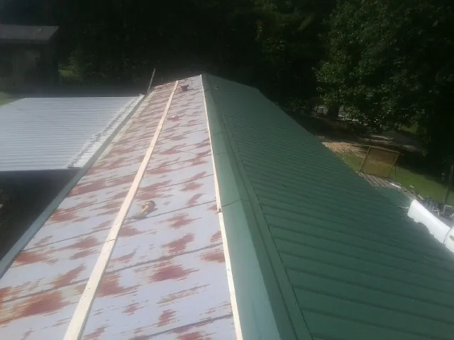 Old rusted panels beside newly installed green metal roofing — Wind Damage Roof Repair by Roofing Brothers in Purdys