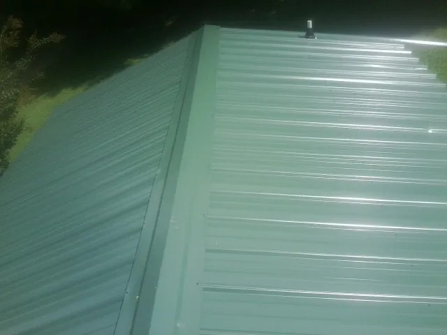 New green metal panels meeting at the ridge of a roof — Flat Roof Repair work by our crew in Purdys