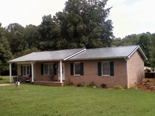 Gray metal roof on a brick ranch house with a side carport in Purdys