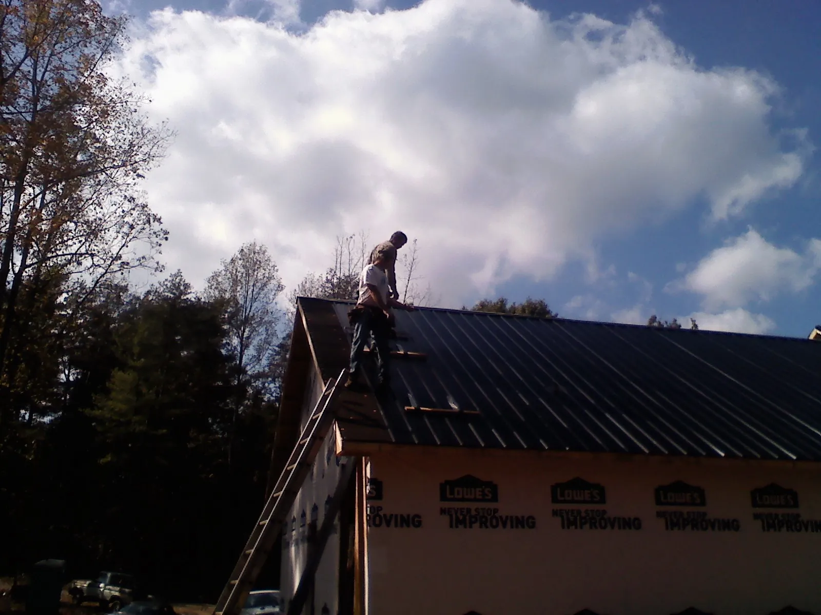 Roofer fastening dark metal panels high against a cloudy sky, from a Roof Inspection job in Purdys