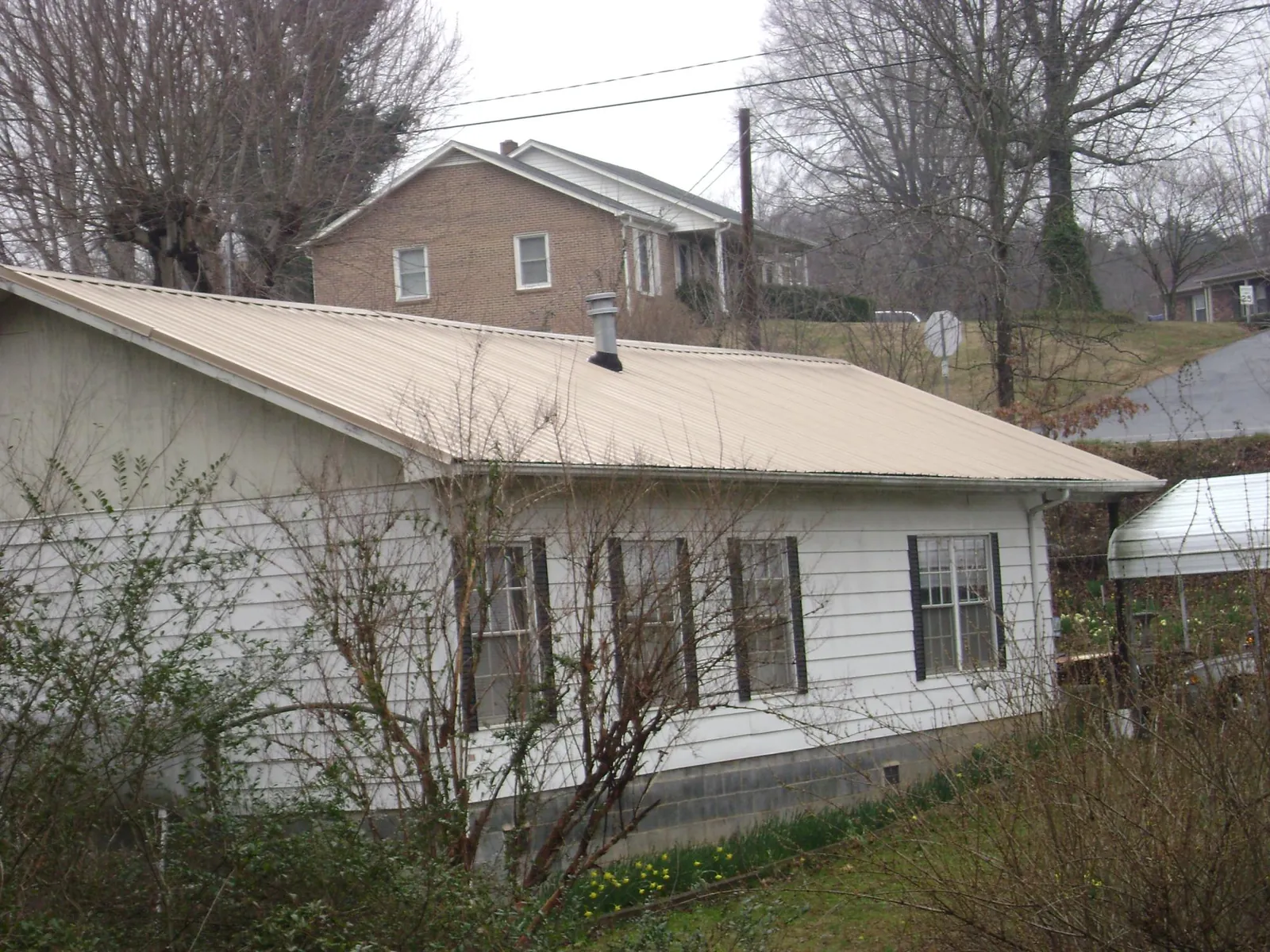 Tan metal roof on a white sided house set into a hillside — Commercial Roofing by Roofing Brothers in Purdys